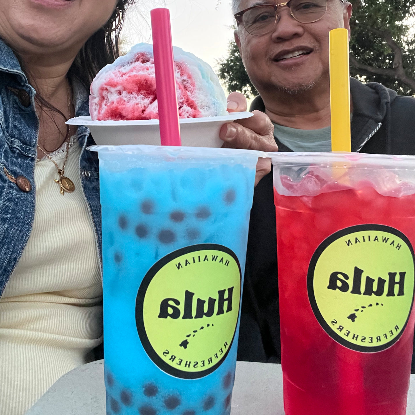 Two large Hula refreshers, blue with boba and red over ice, held up beside a shave ice